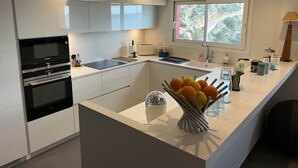 Une cuisine moderne avec des meubles blancs, un four encastré, un évier et une fenêtre donnant sur un espace verdoyant.