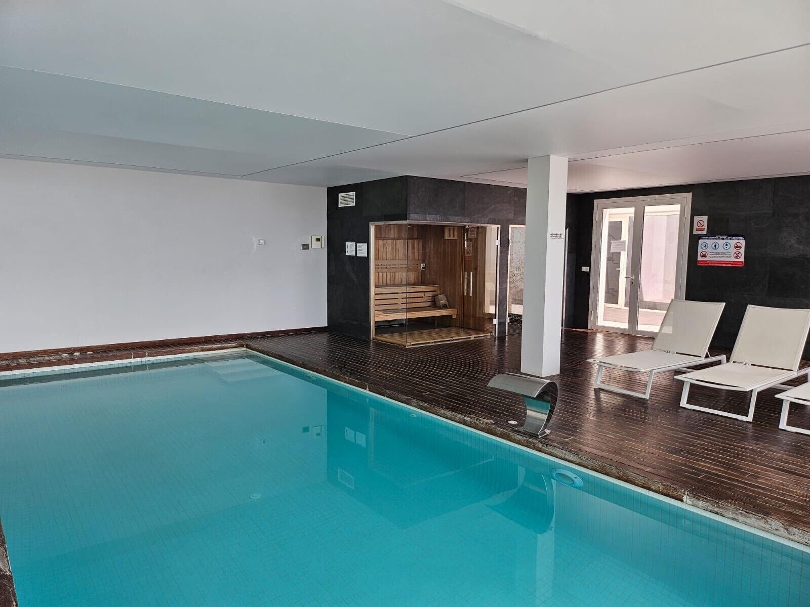 A swimming pool with a wooden deck, a sauna, and white lounge chairs.