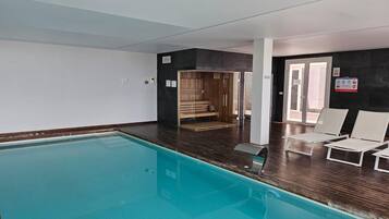A swimming pool with a wooden deck, a sauna, and white lounge chairs.
