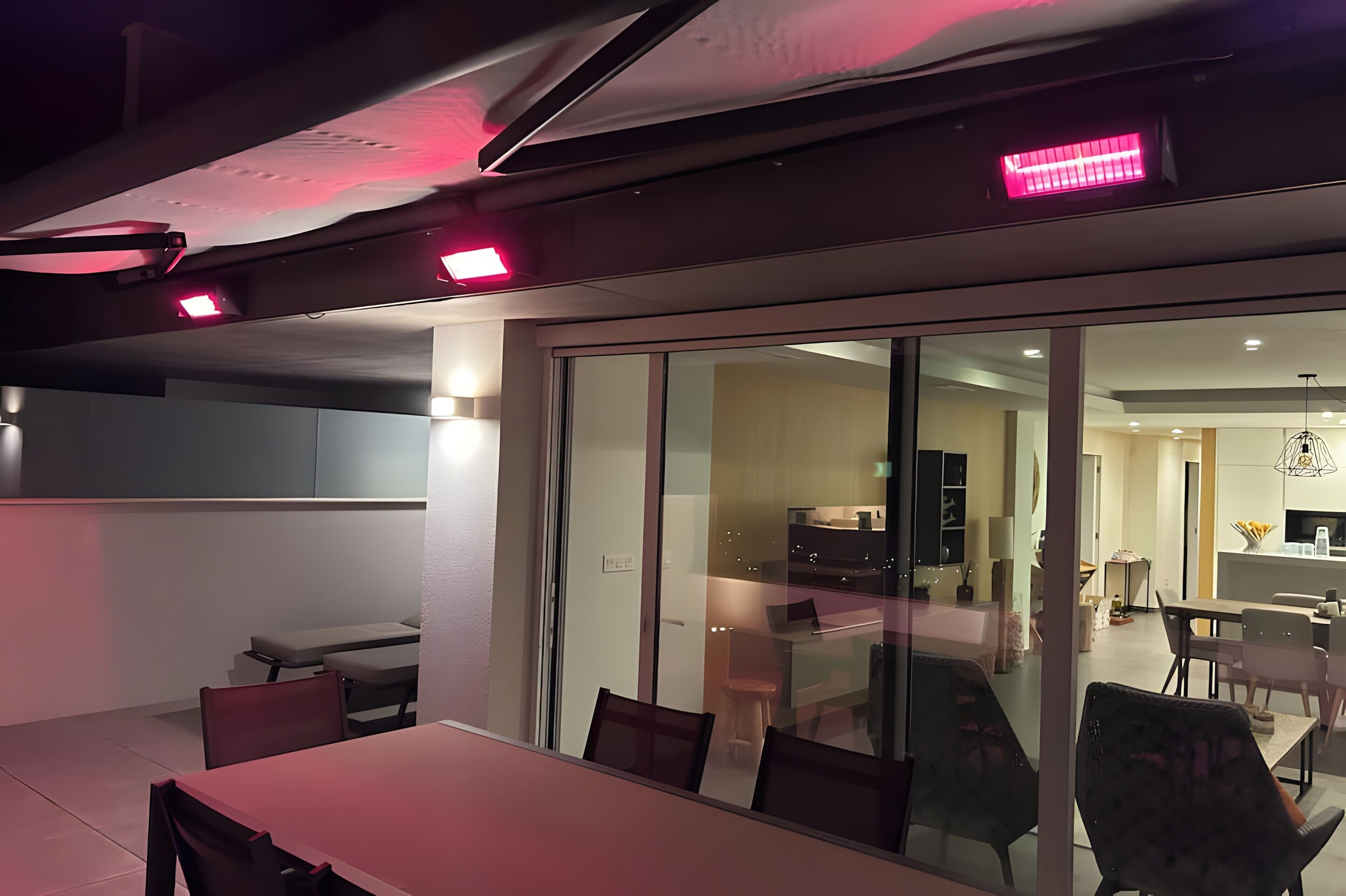 A modern interior with a dining area, a kitchen visible through glass doors, and a ceiling with recessed lighting.