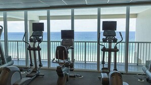 Une salle de sport équipée de machines de cardio et offrant une vue sur l’océan.