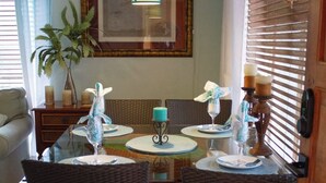 A dining area with wicker chairs, a round glass table, and a hanging light fixture. - Island Comfort 800 Ft. from West Bay Beach — 2BR Gem with Generator (Roatan)