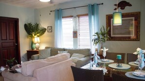 A living room with a sofa, dining table, chairs, and a potted plant. - Island Comfort 800 Ft. from West Bay Beach — 2BR Gem with Generator (Roatan)