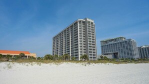A high-rise hotel with multiple balconies, located near a sandy beach.