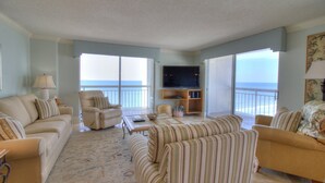 A spacious living room with a large TV, comfortable seating, and a view of the ocean.