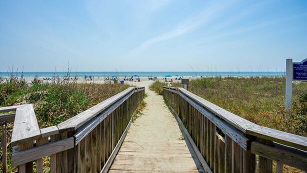 A wooden boardwalk leading to a beach with a clear view of the ocean.