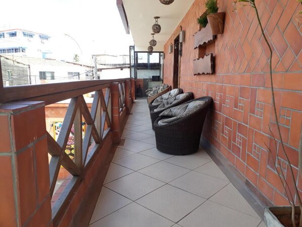 A balcony with wicker furniture, a tiled floor, and a brick wall with decorative elements. - Pousada Aconchego do Porto (Ipojuca)