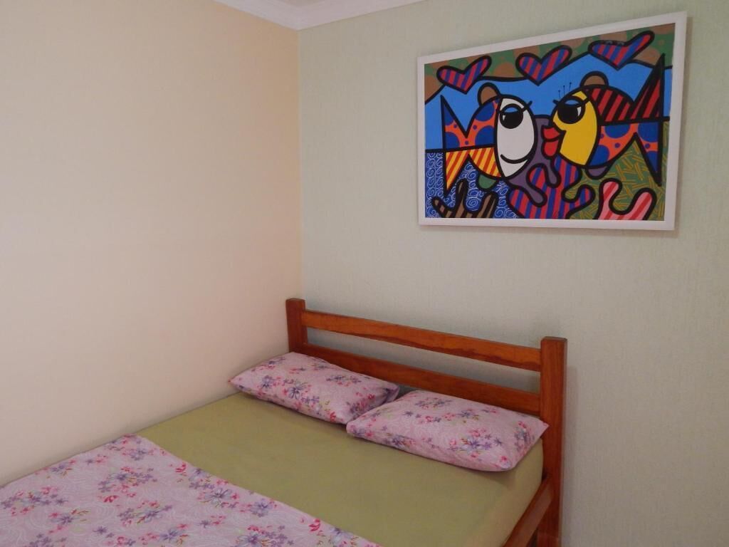 A bedroom with a wooden bed, floral bedding, and a colorful painting on the wall.