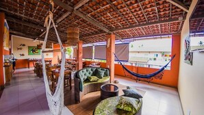 A spacious indoor area with a high ceiling, a hammock, wicker furniture, and a view of the outside. - Pousada Aconchego do Porto (Ipojuca)