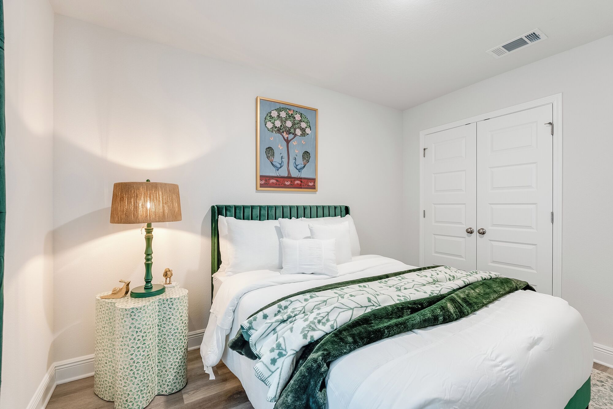 Un dormitorio con cama, mesita de noche con lámpara, un adorno en la pared y un armario.