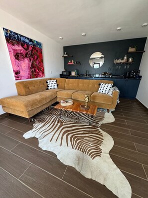 A modern living room with a sectional sofa, a zebra print rug, and a kitchen area with a dark backsplash and a mirror.