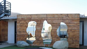 Una estructura de madera con tres espejos y rocas, un pequeño jardín con césped artificial y una escalera.