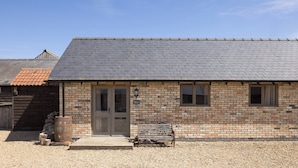 A brick building with a sloped roof, a wooden bench, and a barrel outside. - Stylish cottages, countryside views, wood burning hot tubs, 20 mins to Cambridge (Royston)