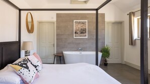 A modern bedroom with a large bed, a sitting area, a bathtub, and a mirror. - Stylish cottages, countryside views, wood burning hot tubs, 20 mins to Cambridge (Royston)