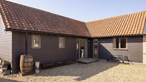 A two-story building with a brown tiled roof, wooden siding, and a gravel driveway. - Stylish cottage, countryside views, wood burning hot tub, 20 mins to Cambridge (Royston)