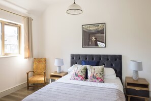 A bedroom with a large bed, two bedside tables, a chair, a window, and a ceiling light.