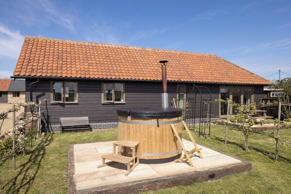 A house with a tiled roof, a hot tub, a wooden bench, and a small table in the yard.