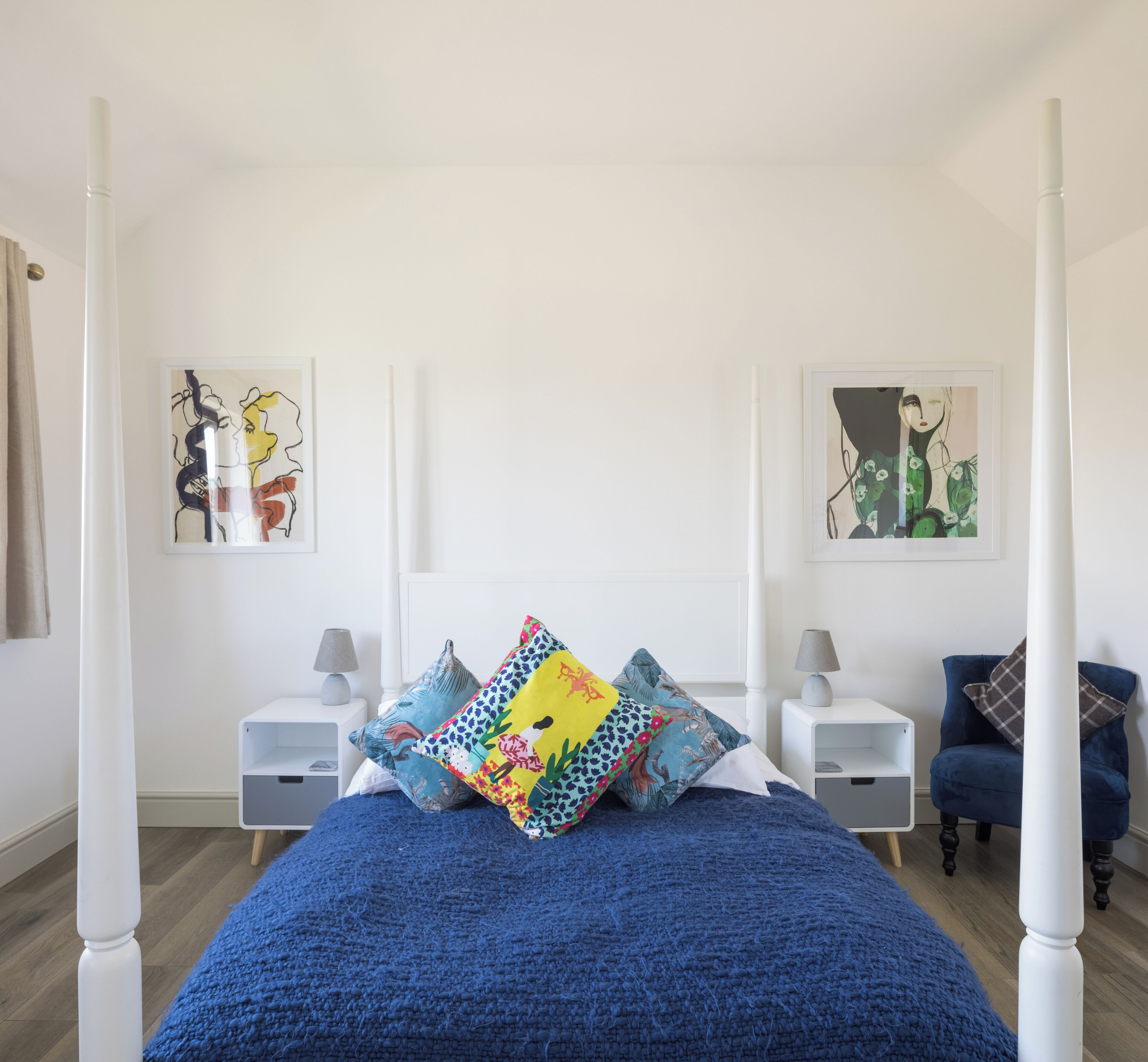 Een slaapkamer met een hemelbed, twee nachtkastjes met lampen, en twee ingelijste kunstwerken aan de wanden.