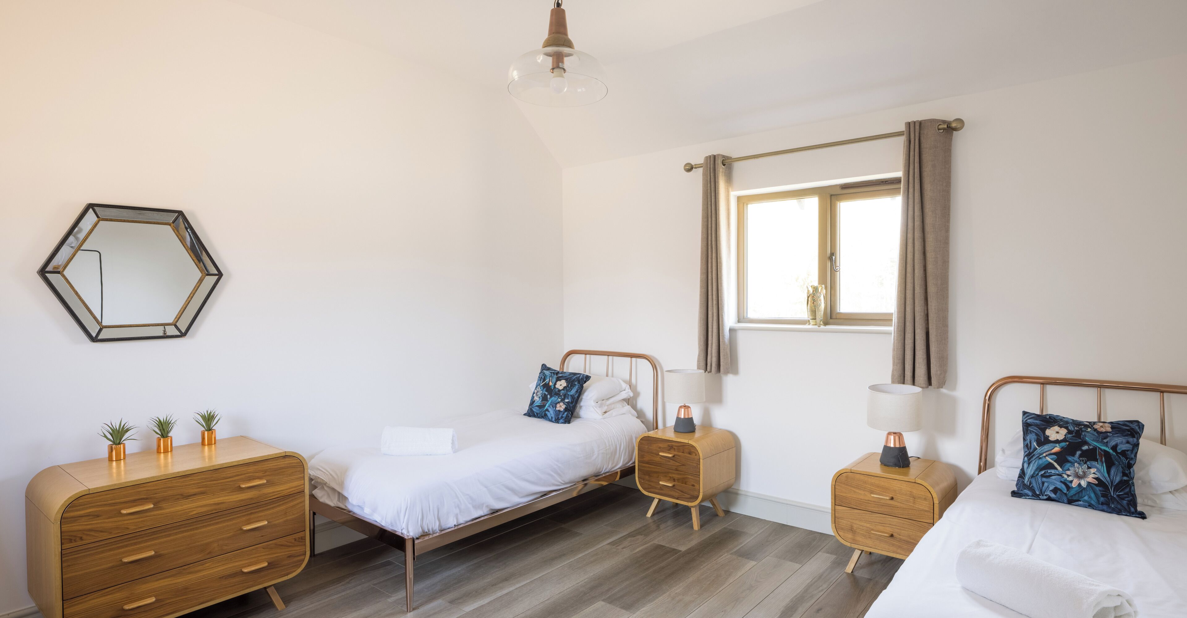 Un dormitorio con una cama, dos mesitas de noche, un aparador, un espejo y una ventana con cortinas.