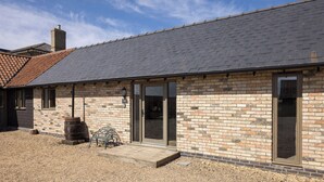 Un bâtiment en briques avec un toit en pente, une terrasse en bois et un tonneau.