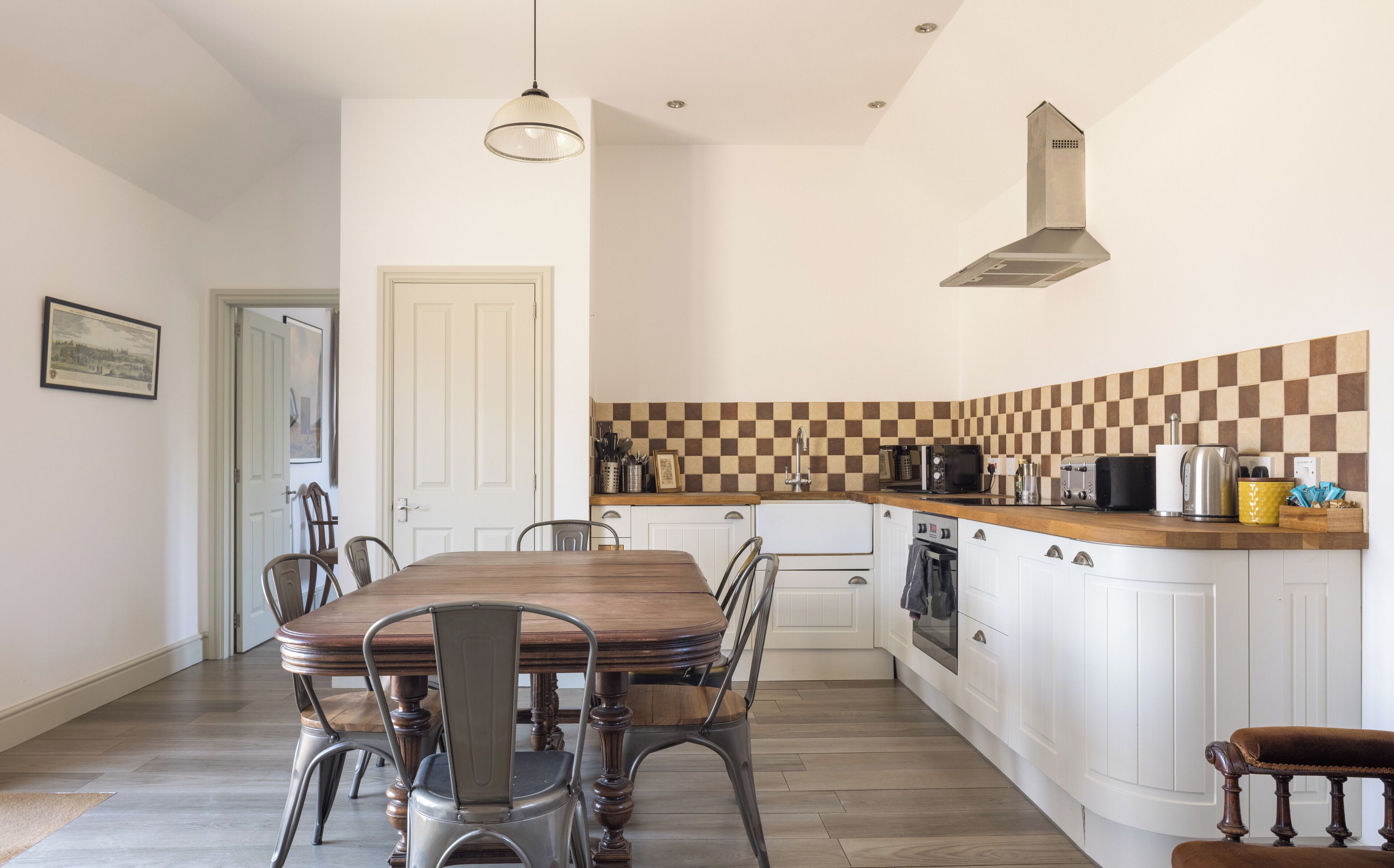 A kitchen with a wooden dining table, white cabinets, and a checkered backsplash.