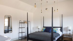 Une chambre à coucher moderne avec un lit à baldaquin, une table de chevet, une commode, un miroir et un luminaire suspendu.