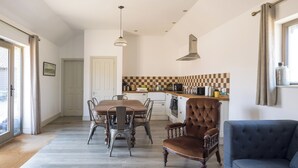 Une cuisine moderne avec un coin repas, comprenant un crédence à carreaux, une grande fenêtre avec des rideaux et un fauteuil bleu.
