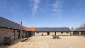 A building with a gravel courtyard, a wooden barrel, and a stone wall. - Stylish cottages, countryside views, wood burning hot tubs, 20 mins to Cambridge (Royston)