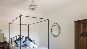 A four-poster bed with a light blue bedspread and decorative pillows, a wooden dresser, a mirror, and a chandelier. - Stylish cottage, courtyard views, countryside location, 20 mins to Cambridge (Royston)