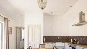 A modern kitchen with a wooden dining table, chairs, a chandelier, and a tiled backsplash. - Stylish cottage, courtyard views, countryside location, 20 mins to Cambridge (Royston)