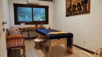 Une pièce comprenant une table de massage, un banc en bois, un petit tabouret et un tableau accroché au mur.