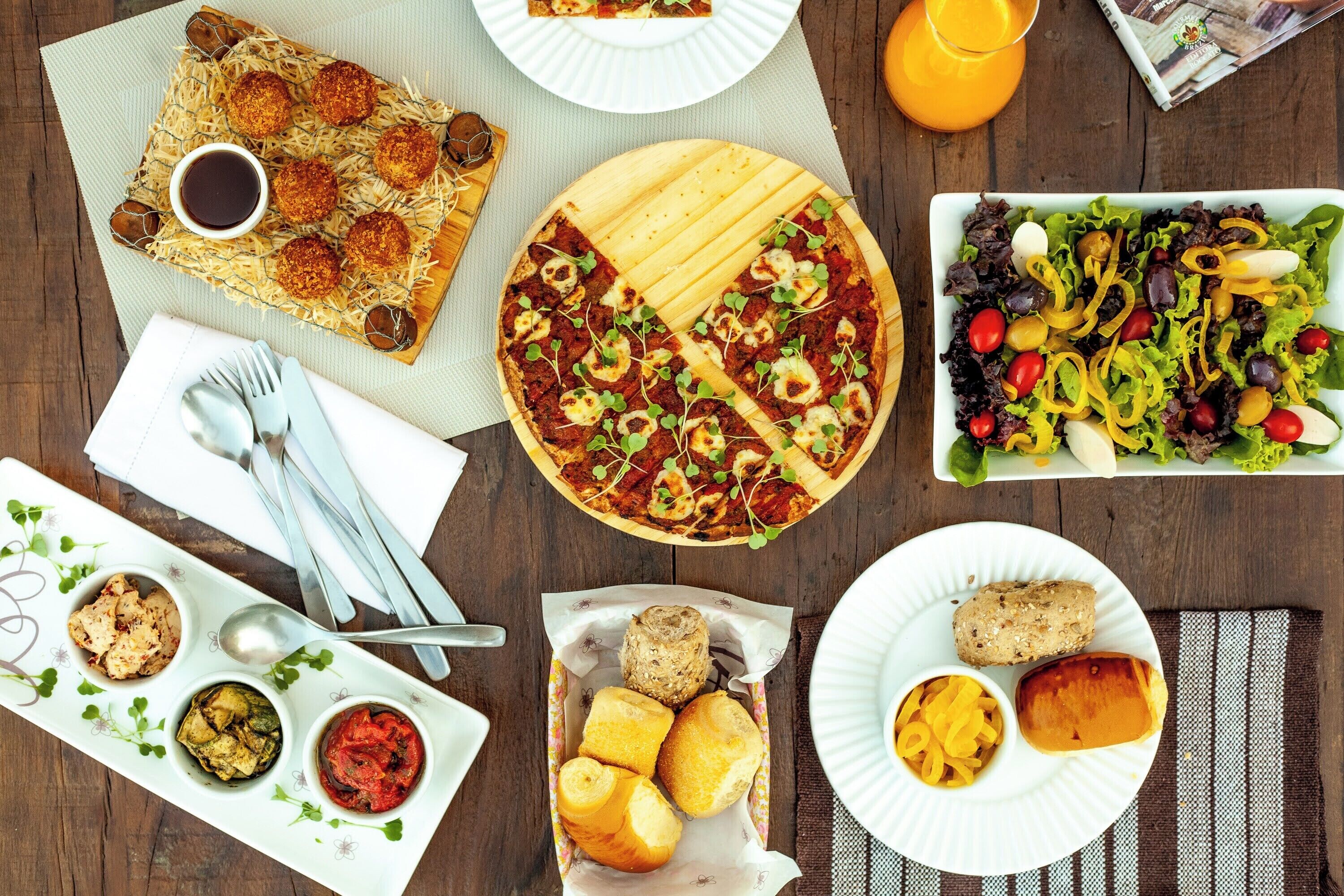Ein Tisch mit verschiedenen Speisen, darunter Pizza, Salat und Brot.