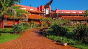 A red-brick building with a unique angular roof structure, surrounded by lush greenery and a paved walkway. - Frangipani Hotel Boutique (Brotas)
