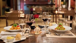 A dining table set with plates of pasta, wine glasses, a vase with a rose, and a bottle of wine. - Frangipani Hotel Boutique (Brotas)