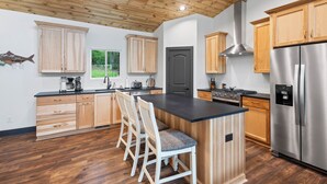 A modern kitchen with wooden cabinets, a stainless steel refrigerator, and a central island with bar stools.