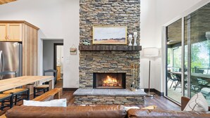 A modern living room with a stone fireplace, leather sofa, and a dining area with wooden furniture.