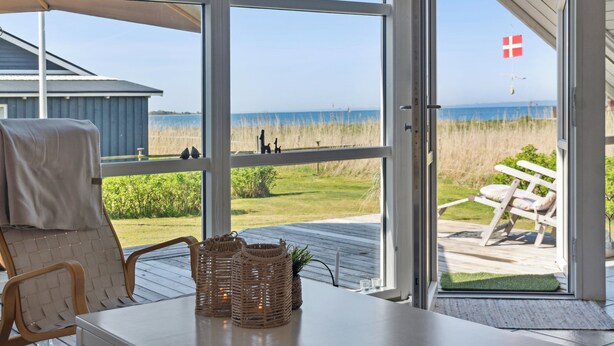 A room with a view of the beach, a wicker basket, a chair, and a table.