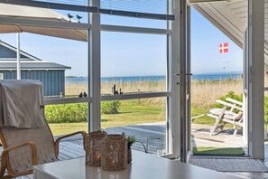 A room with a view of the beach, a wicker basket, a chair, and a table.