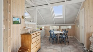 A room with a high ceiling, wooden walls, a dining table with chairs, a wooden dresser, and a window with a view.