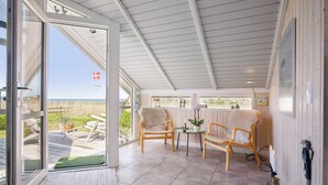 A room with a large sliding glass door leading to a deck, two wooden chairs, a small table with a plant, and a wall-mounted light fixture.
