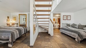 A bedroom with two beds, a staircase, and a hallway leading to another room. - Sea and meadow views – space and calm (Nyborg)