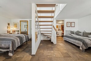 A bedroom with two beds, a staircase, and a hallway leading to another room.