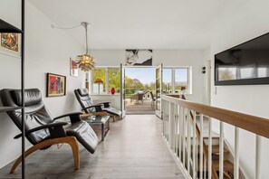 A modern interior with a view to the outdoors, featuring leather chairs, a wooden table, and a staircase.