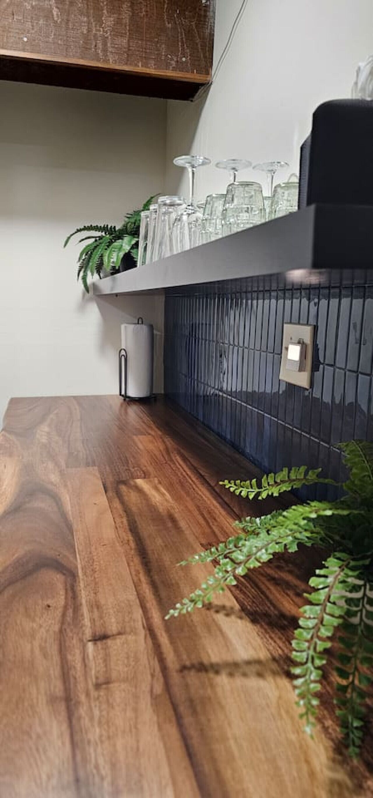 A wooden table with a tiled backsplash, a potted plant, and a glass container on the shelf.