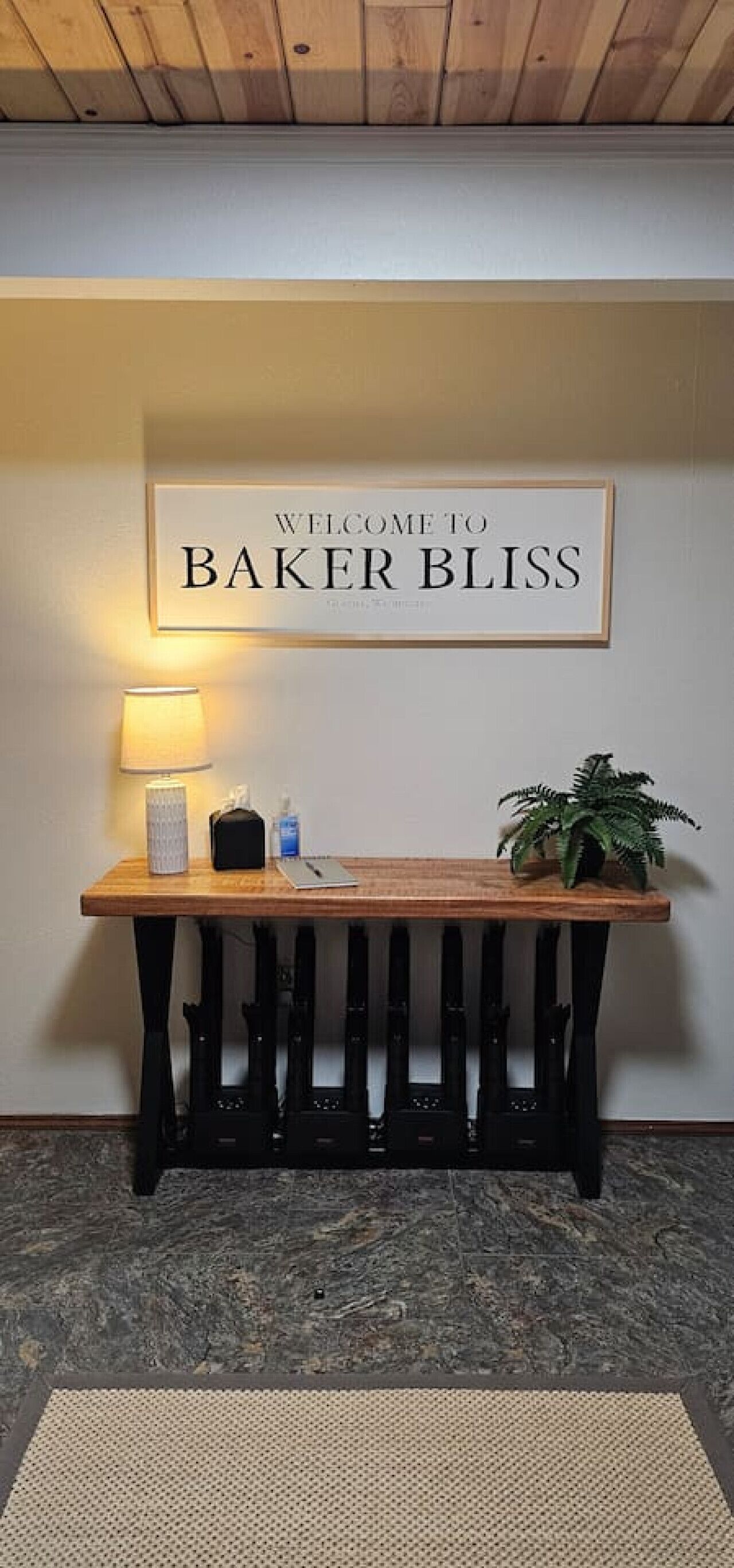 A reception area with a wooden table, a lamp, a potted plant, and a welcome sign.