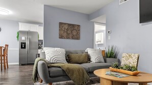 A modern living room with a grey sofa, a wooden coffee table, and a kitchen area in the background.