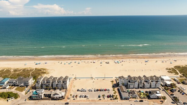 A coastal hotel with a beach view, parking lots, and a row of similar buildings.