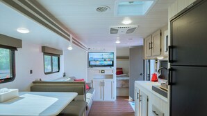 A compact RV interior with a dining area, kitchenette, and a TV mounted on the wall. - Gramercy Village Yamanakako (Yamanakako)