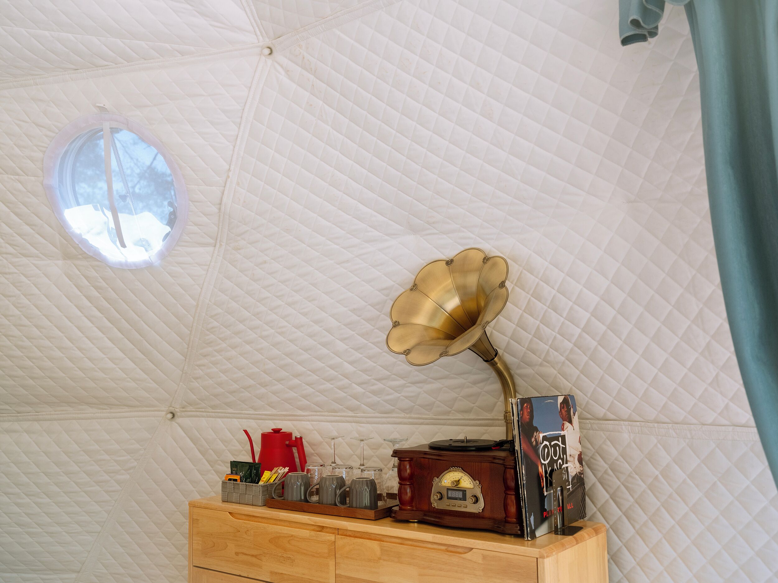 A cozy room with a quilted dome ceiling, a wooden dresser, a gramophone, and a small window.