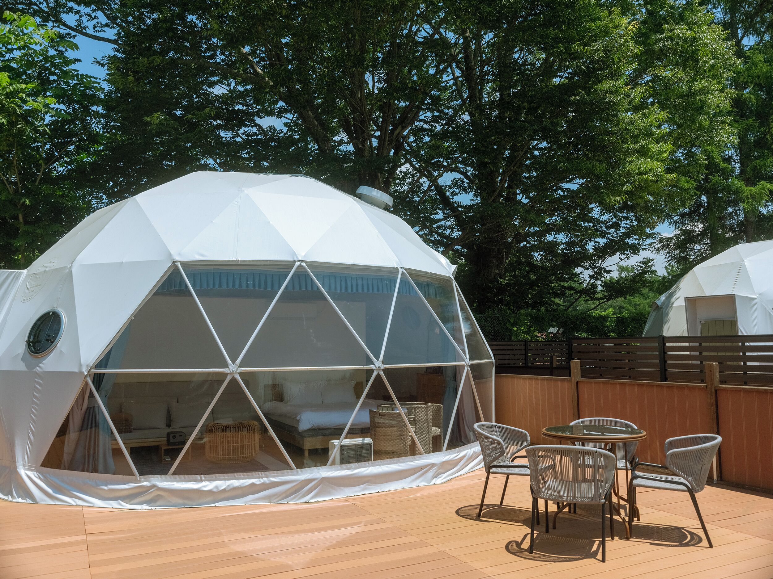 A geodesic dome structure with a transparent section revealing a bed and a small table with chairs.